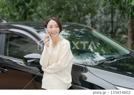 車の前に立って電話をする女性 135654602