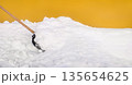 Snow shovel scooping fresh snow against a vibrant yellow wall 135654625