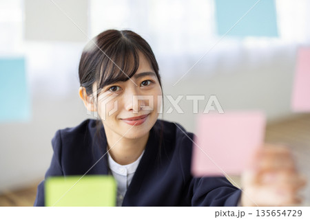 オフィスで付箋を手に微笑むスーツを着た若い女性 オフィスで付箋を手に微笑むスーツを着た若い女性 135654729