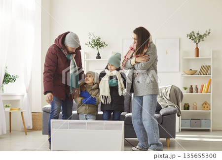Family With Children Warming By Electric Heater At Home In Winter 135655300