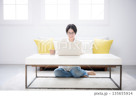 部屋でニットを着てスマホをタップ、見るショートカットの女性　春秋冬の優しい明るいイメージ	 135655914