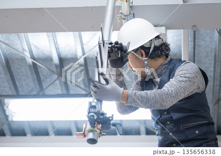 天井が近い高所の足場で単管パイプを組み立てる、固定するクランプなどの施工作業　髭の鳶職や作業員、現場 135656338