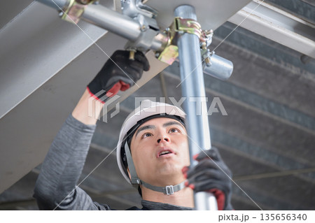 天井が近い高所の足場で単管パイプを固定するクランプなどの施工作業 鳶職や作業員のイメージ レンチ 天井が近い高所の足場で単管パイプを固定するクランプなどの施工作業 鳶職や作業員のイメージ レンチ 135656340