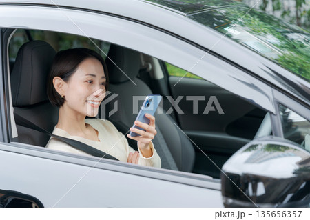運転席でスマホを見る女性 135656357
