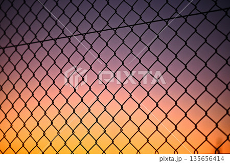 夕暮れの空と金網フェンス 135656414