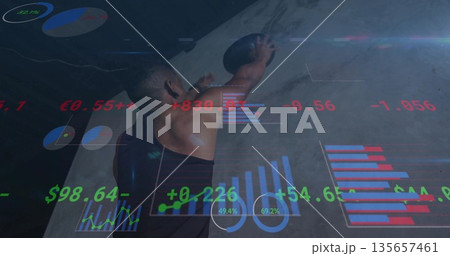 Athlete in tank top lifting medicine ball overhead against gym wall, with holographic charts 135657461