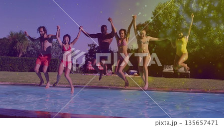 Jumping group of six friends holding hands at backyard pool, with swimsuits and inflatable ball 135657471