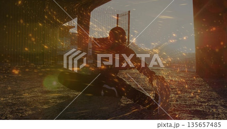 Dancing man in hoodie weaving spark-like lights on gravel under overpass pillars, fence at dusk 135657485