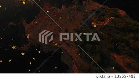 Hovering golden star-shaped graphics above rocky coastal cliff at night, with shrubs and dark water 135657488
