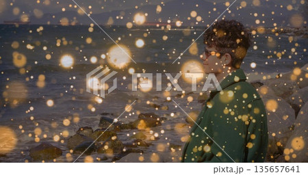 Standing man wearing overcoat facing rocky shore with cargo ships and golden lights, copy space Standing man wearing overcoat facing rocky shore with cargo ships and golden lights, copy space 135657641