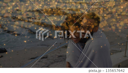 Leaning against metal railing at seaside promenade, woman and man wrapping in light-colored blanket Leaning against metal railing at seaside promenade, woman and man wrapping in light-colored blanket 135657642