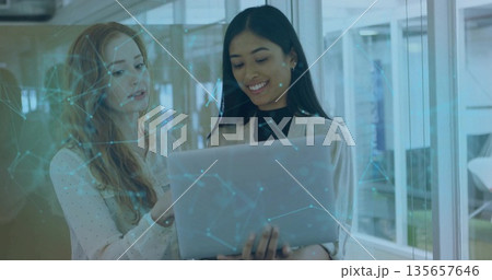 Collaborating two tech professionals wearing blazer examining laptop in office with network overlay 135657646