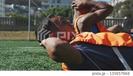 Performing sit-up exercises soccer players lying on turf field, with training bibs, athletic shorts 135657668