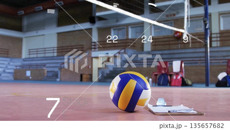 Lying volleyball beside clipboard and pen on gymnasium court, with net posts and red chairs 135657682