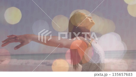 Stretching arms woman in sleeveless tank top under bokeh effect at sandy shoreline, waves rolling 135657683
