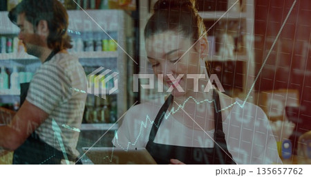 Tapping tablet employee wearing black apron at cafe, with jars and cans on shelves Tapping tablet employee wearing black apron at cafe, with jars and cans on shelves 135657762