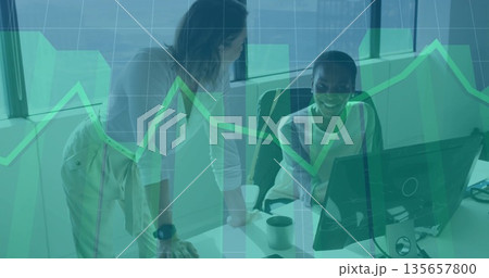 Leaning women in business casual reviewing charts at office desk, with PC monitor and smartphone Leaning women in business casual reviewing charts at office desk, with PC monitor and smartphone 135657800