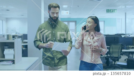 Walking colleagues in business attire in office, carrying documents while speaking into smartphone Walking colleagues in business attire in office, carrying documents while speaking into smartphone 135657810