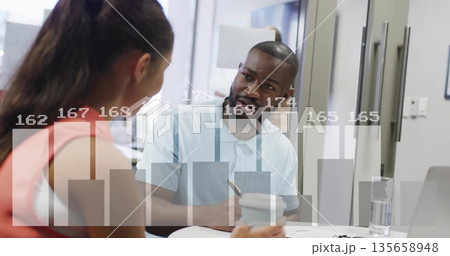 Two coworkers discussing project data in conference room, with printed documents and chart overlay Two coworkers discussing project data in conference room, with printed documents and chart overlay 135658948