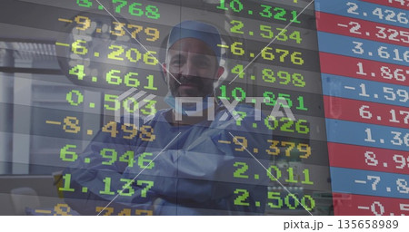 Surgeon wearing surgical attire crossing arms inside OR, frosted glass and financial overlay Surgeon wearing surgical attire crossing arms inside OR, frosted glass and financial overlay 135658989