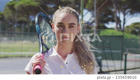 Standing woman wearing white shirt holding pink-gripped racket on tennis hardcourt, with windscreen Standing woman wearing white shirt holding pink-gripped racket on tennis hardcourt, with windscreen 135659010