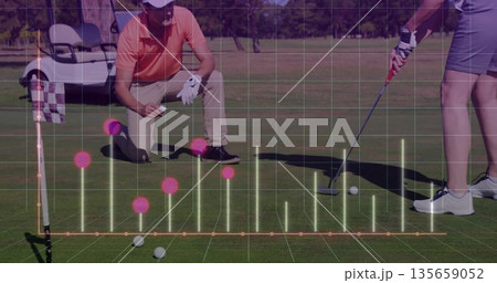 Standing woman lining up putt on sunlit green with crouching partner checking line via AR overlay 135659052