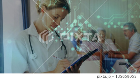 Writing female doctor with stethoscope noting clipboard in clinic with seniors at table, copy space Writing female doctor with stethoscope noting clipboard in clinic with seniors at table, copy space 135659055
