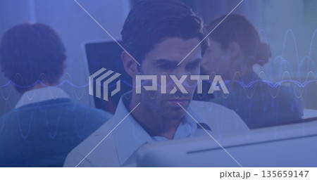 Working mid adult man in blue shirt analyzing audio waveform at monitor in open-plan office 135659147