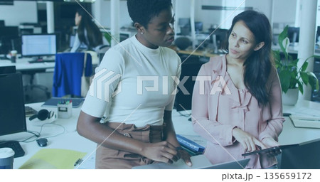 Collaborating women in business attire discussing project at office desk, with laptop and tablet Collaborating women in business attire discussing project at office desk, with laptop and tablet 135659172