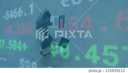 Walking business professionals checking market data on laptops across office lobby, stock overlay 135659213