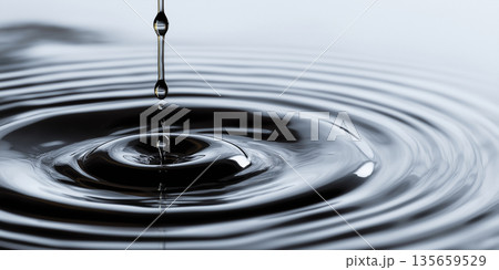 Close-up of water droplet creating ripples on a smooth surface, with a soft gradient background enhancing the fluid motion and reflective qualities of the water 135659529