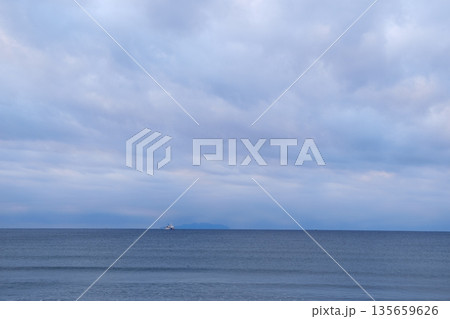 曇り空の下に広がる静かな海と沖に停泊いている大型船 曇り空の下に広がる静かな海と沖に停泊いている大型船 135659626