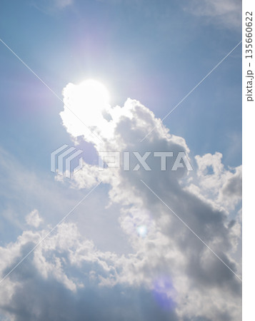 Sun shining brightly through a gap in the white cumulus clouds in a blue sky. Natural light background for weather forecast. 135660622
