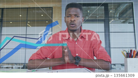 Sitting man wearing red shirt and wristwatch at desk with glass partitions papers chart overlays 135661309