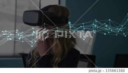Adjusting woman wearing blazer and VR headset in conference room, with network overlay, copy space 135661380
