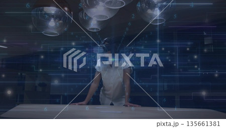 Leaning adult woman wearing VR headset using holographic UI in tech lab, with pendant lights 135661381