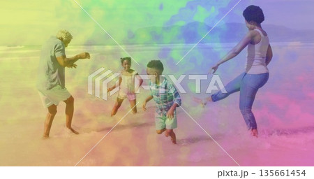 Splashing family wearing beachwear and kicking shallow ocean water on sandy beach, with small waves 135661454