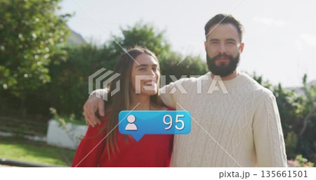 Smiling couple wearing cozy red and cream sweaters posing in garden, with blue notification bubble 135661501