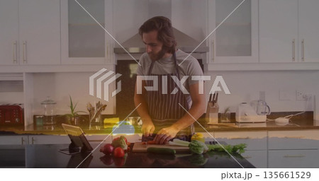 Chopping man wearing striped apron cutting produce in modern kitchen, with cutting board and tablet Chopping man wearing striped apron cutting produce in modern kitchen, with cutting board and tablet 135661529
