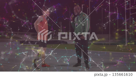 Coach interviewing athlete in sportswear on track at night with microphone and prosthetic blade 135661610