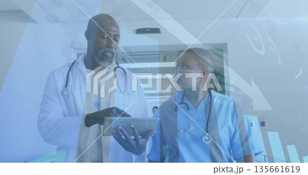Walking lab coat doctor and scrubs nurse with stethoscopes reviewing tablet in hospital corridor Walking lab coat doctor and scrubs nurse with stethoscopes reviewing tablet in hospital corridor 135661619