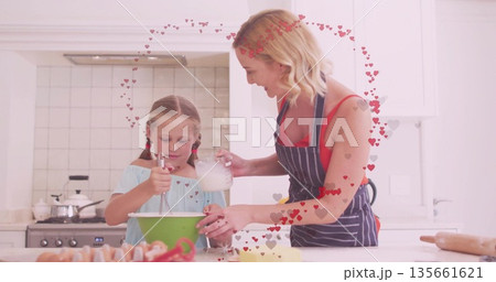 Mother in apron stirring batter and pouring milk with daughter at white countertop, green bowl Mother in apron stirring batter and pouring milk with daughter at white countertop, green bowl 135661621