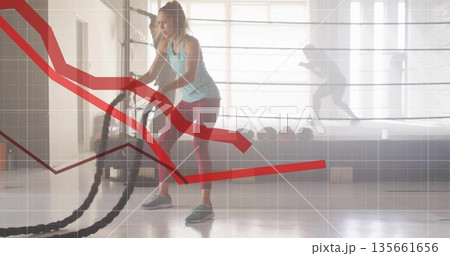 Swinging trainee in athletic wear gripping battle ropes in studio, with boxing ring and data charts 135661656