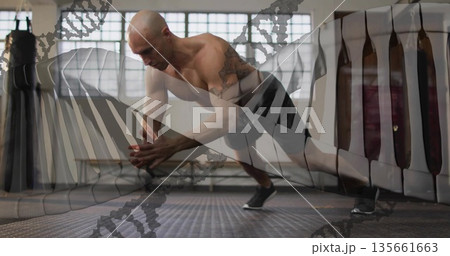 Lunging shirtless man balancing on one leg in fitness studio, with punching bag and padded targets 135661663