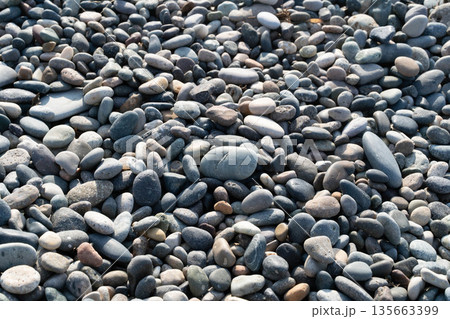 A serene coastal scene showcases smooth, colorful pebbles under bright sunlight. This luxurious setting invites relaxation, ideal for spa treatments by the sea. 135663399