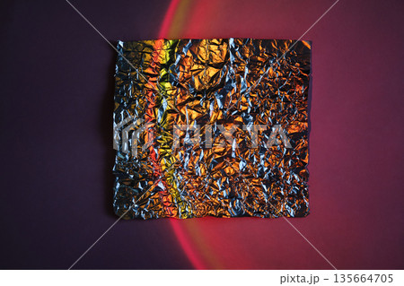 Crumpled metallic foil square on abstract neon gradient background with red light arc 135664705