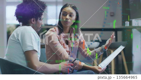 Business colleagues discussing financial data on tablet in office lounge, with candlestick overlays 135664965