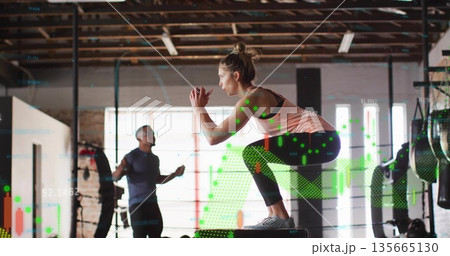 Crouching woman athlete performing squat on plyometric box in brick gym, with digital data overlay Crouching woman athlete performing squat on plyometric box in brick gym, with digital data overlay 135665130