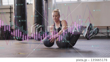 Doing V-sit core exercise female athlete lifting medicine ball at gym studio, with chart overlay Doing V-sit core exercise female athlete lifting medicine ball at gym studio, with chart overlay 135665178
