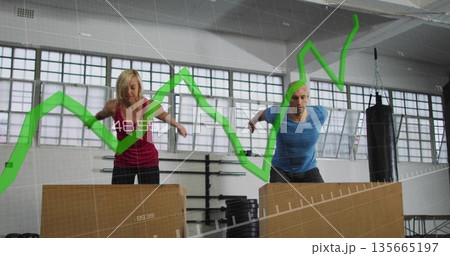 Workout partners performing box jumps in gym studio, with plyometric boxes and green graph overlay 135665197